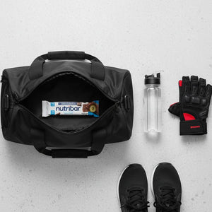 Black duffel bag with Nutribar, water bottle, and gloves on a light gray surface