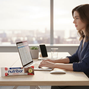 Woman working at a desk with a laptop and Nutribar on a table.