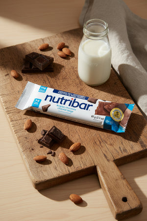 Nutribar chocolate flavor bar on a wooden cutting board with a bottle of milk and nuts.