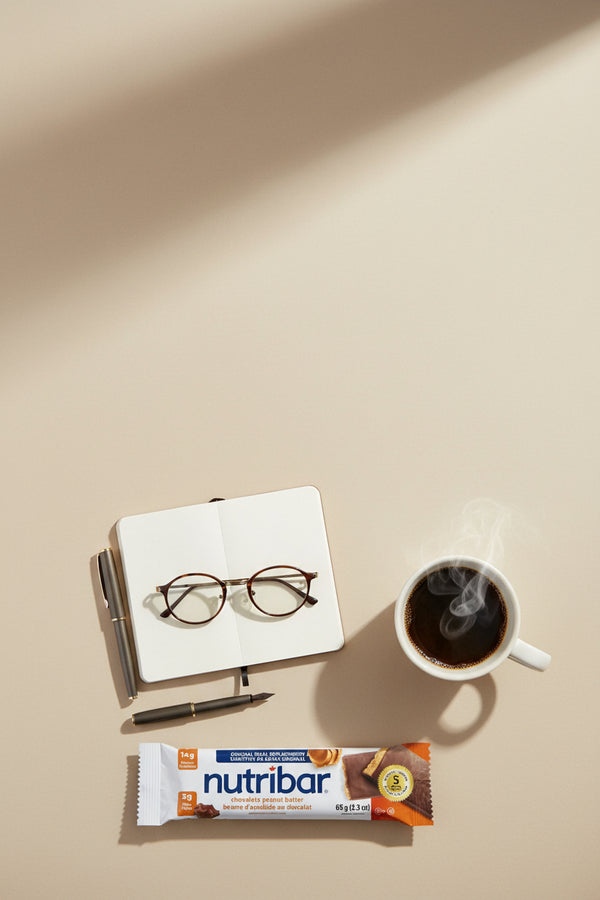 Nutribar with a cup of coffee, glasses, and a notebook on a beige surface