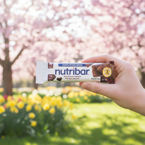 Hand holding a Nutribar in front of cherry blossom trees and yellow flowers