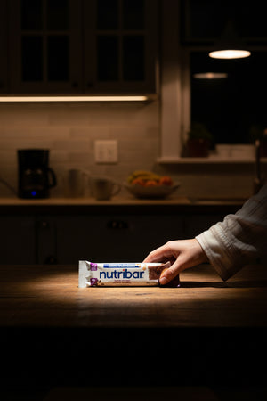 Hand holding a Nutribar package on a kitchen counter with dim lighting