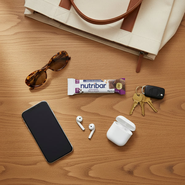 Phone, earbuds, nutribar, keys, and sunglasses on a wooden surface with a beige bag.